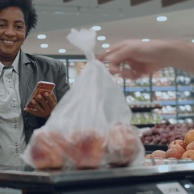 Cliente acompanhando a pesagem de frutas em balança no setor de FLV de um supermercado.